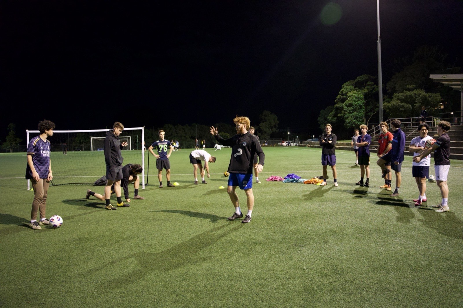 The host chatting with players gathered in a loose circle on the pitch before kick-off