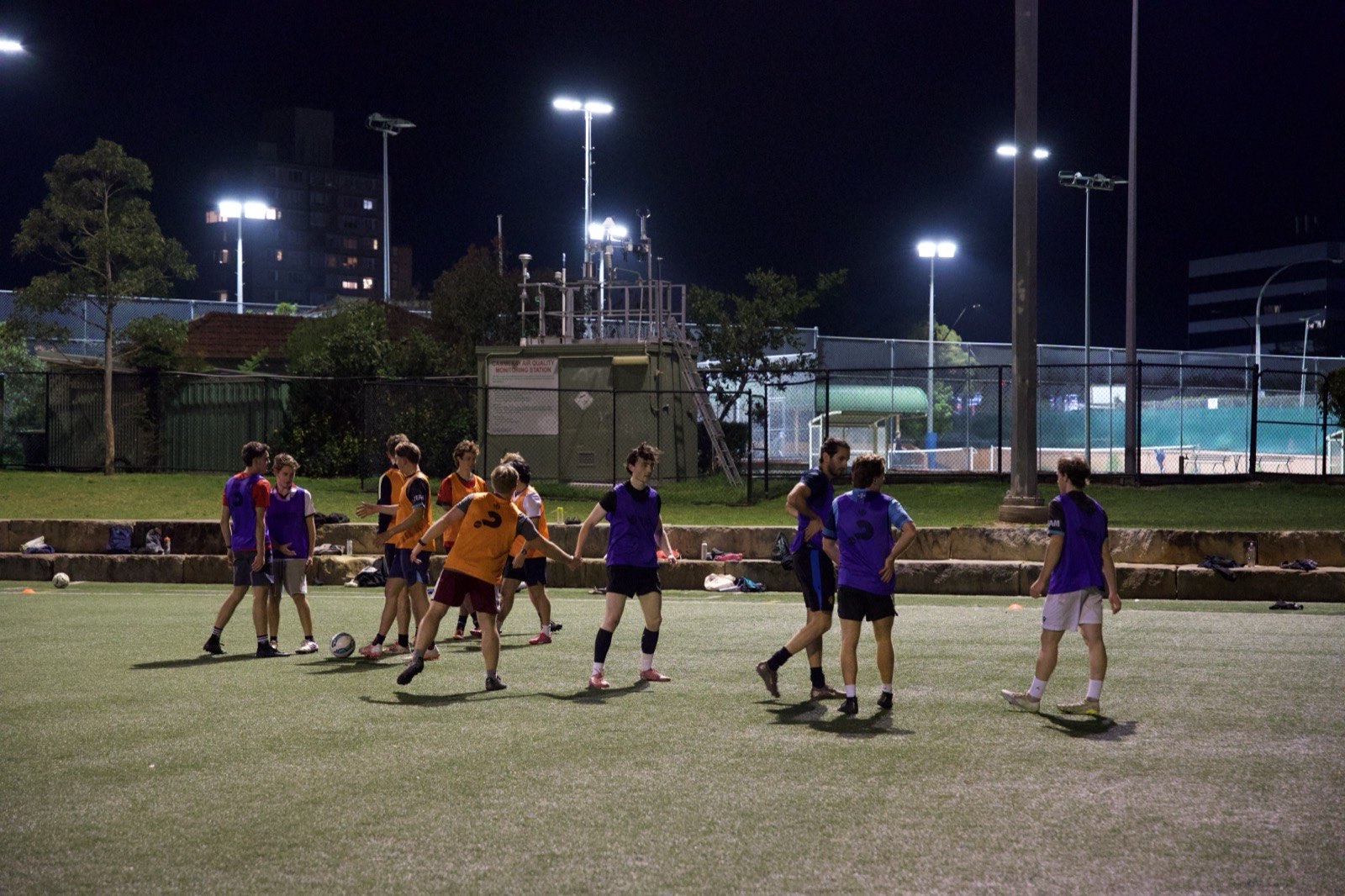 A small-sided game in coloured bibs on a floodlit pitch at night