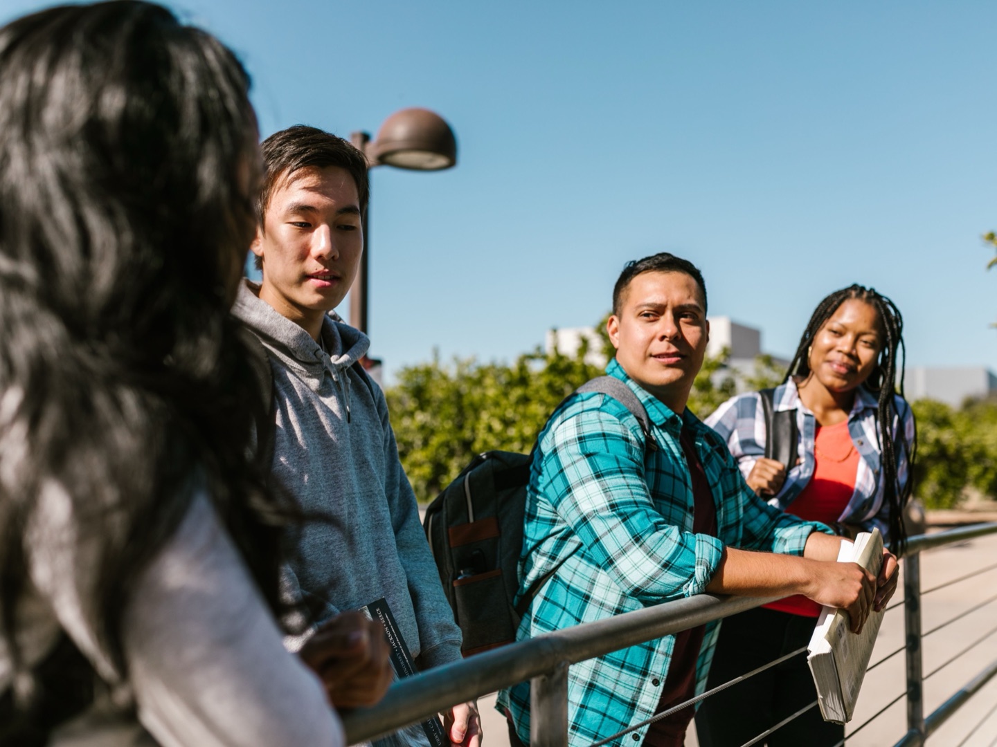 Four students leaning on a railing in the sun, mid-conversation