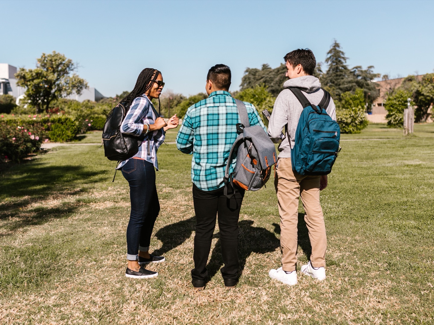 Three students with backpacks standing on a campus lawn, chatting